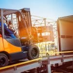 Forklift is putting cargo from warehouse to truck outdoors